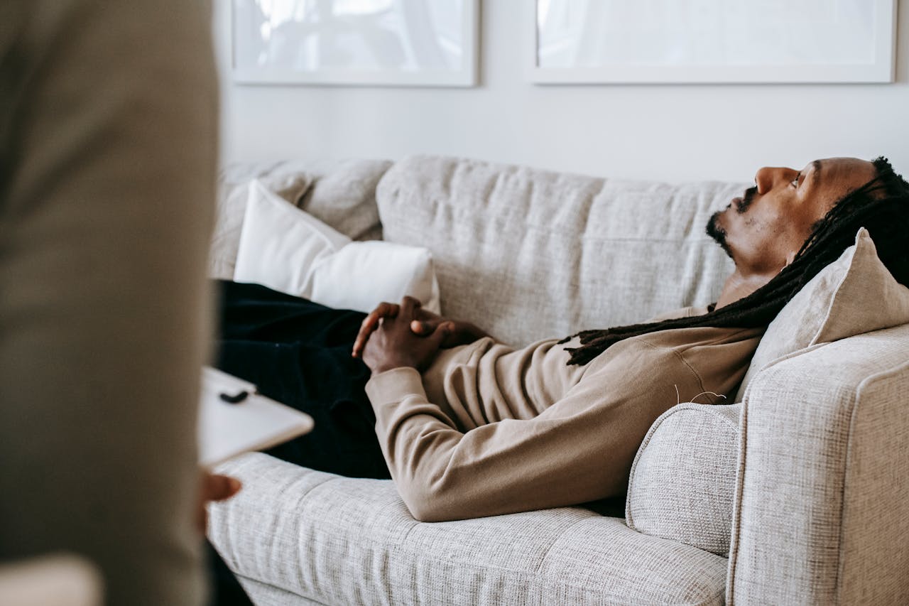 Man in therapy session lying on sofa, conversing with therapist in a relaxed indoor setting.